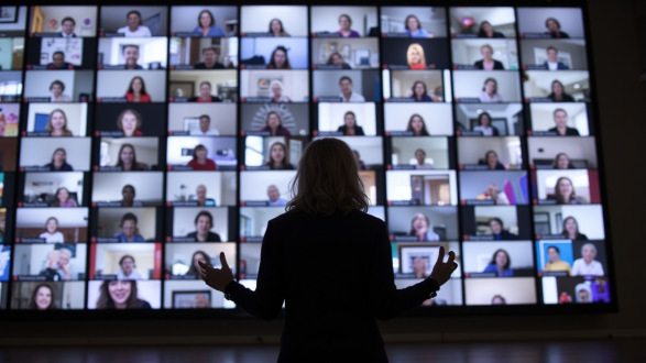 Silhouetted woman presenting to a giant video wall filled with dozens of virtual attendees